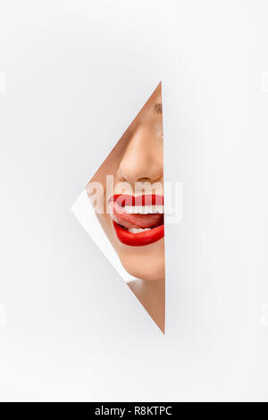 Cropped shot of girl licking lèvres dans le trou on white Banque D'Images