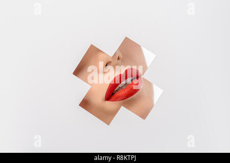 Cropped shot of young woman with red lips à travers le trou en forme de croix sur blanc Banque D'Images