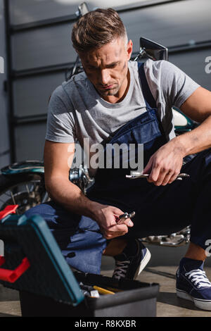 Handsome mechanic picking clés pour moto dans garage fixation Banque D'Images