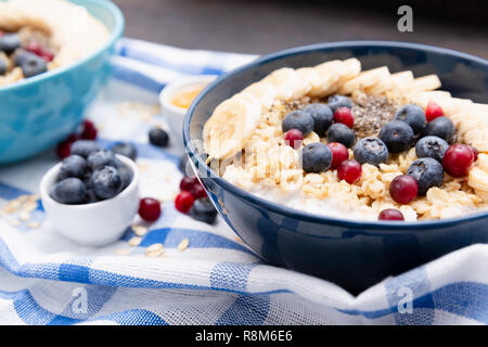 Petit-déjeuner de remise en forme en bonne santé : avoine avec les bananes, les bleuets et les canneberges, amandes et noix et yaourt sur serviette bleu et blanc Banque D'Images