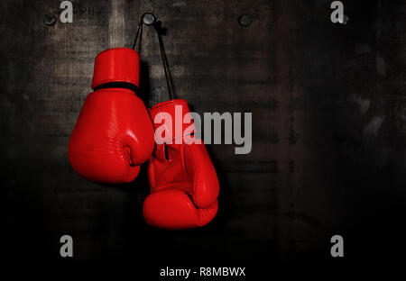 Close up paire de gants de boxe en cuir rouge suspendue au-dessus de mur noir with copy space Banque D'Images