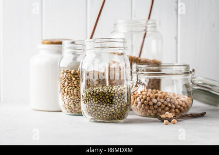 Plusieurs légumineuses : haricots, pois chiches, le sarrasin, les lentilles dans des bocaux en verre sur un fond blanc. L'alimentation végétarienne saine, protéines végétales, mourir à base de plantes Banque D'Images