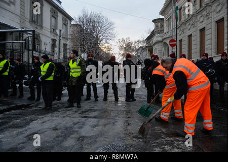 Budapest, Hongrie. Dec 16, 2018. Les travailleurs de la ville sont vus retirer des blocs de glace à partir de la chaussée en tant qu'agents de police de prendre des mesures de sécurité au cours de la protestation contre la nouvelle législation du travail approuvé par l'aile droite du gouvernement conservateur dirigé par Vikotor Orban.Le Gouvernement hongrois a adopté un ensemble de lois controversées sur l'entraide judiciaire et du travail sujets, la nouvelle loi sur le travail, connu sous le nom de ''slave'' de la loi permet aux employeurs de demander à leurs travailleurs de prendre sur jusqu'à 400 heures supplémentaires par an. Credit : Omar Marques/SOPA Images/ZUMA/Alamy Fil Live News Banque D'Images