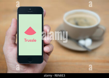 Un homme se penche sur son iPhone qui affiche le logo Trussle (usage éditorial uniquement). Banque D'Images
