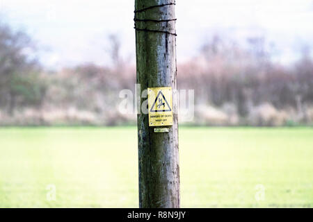 Danger de mort d'électricité avertissement triangulaire contre fond rectangulaire jaune sur poteau télégraphique dans la zone de flou artistique contre l'arrière-plan clair. Banque D'Images