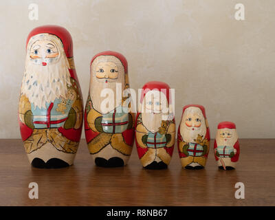 Une famille de poupées en bois peint à la nidification Santa debout dans une ligne holding gifts. Photographié sur une surface en bois au niveau de l'oeil. Banque D'Images