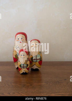 Une famille de trois poupées en bois peint à la nidification Santa debout dans une ligne holding gifts. Photographié sur une surface en bois au niveau de l'oeil. Banque D'Images