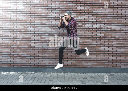 Say Cheese, photographe de mode hippie homme faire une photo avec l'appareil photo rétro en saut. Banque D'Images