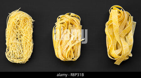 Ensemble de diverses pâtes alimentaires non cuites : fettuccine, pappardelle, tagliolini sombre sur fond noir, vue de dessus. Libre. Banque D'Images