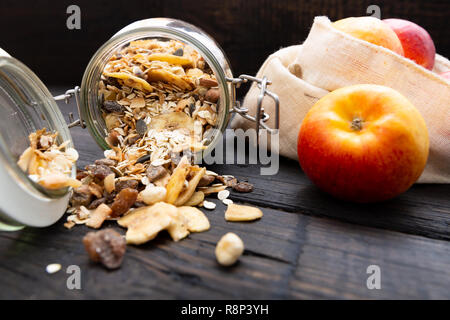 Granola fait maison dans un bocal en verre et les pommes dans un sac en tissu réutilisable sur table en bois foncé avec la texture. Petit-déjeuner sain et concept concept zéro déchet Banque D'Images