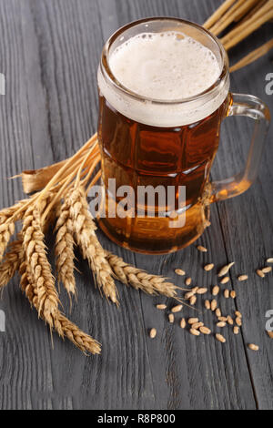 Verre de bière mousseuse avec cônes de houblon et de blé noir sur fond de bois Banque D'Images