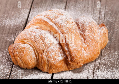 Croissant saupoudrée de sucre en poudre sur la vieille planche de bois Banque D'Images