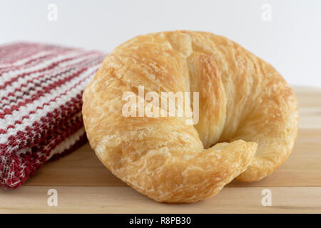 Seul un croissant rouleau sur planche à découper en bois avec une serviette rouge et blanc à proximité. Vue côté macro avec un fond blanc. Banque D'Images