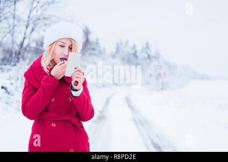 Belle jeune femme appliquant le maquillage à l'extérieur en hiver Banque D'Images