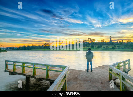 Homme debout sur un petit pont reflétant sur le lac au lever du soleil comme une façon d'accueillir la belle nouvelle journée Banque D'Images