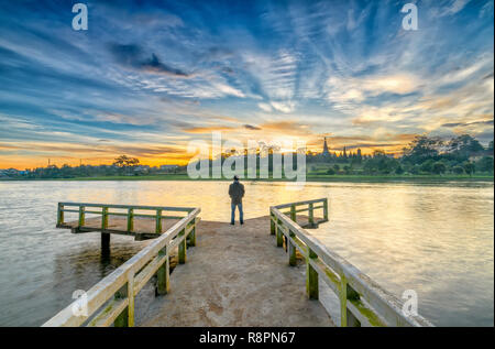 Homme debout sur un petit pont reflétant sur le lac au lever du soleil comme une façon d'accueillir la belle nouvelle journée Banque D'Images