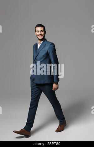 Longueur totale de l'image arabe unshaved man 30s en costume formel isolé marche sur fond gris Banque D'Images
