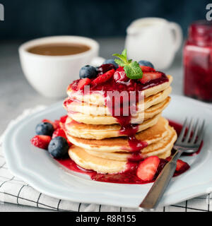 Pile de crêpes avec sauce aux baies, de bleuet, de fraise et de Cranberry. Tasse de café et de crème sur l'arrière-plan. Culture Square Banque D'Images