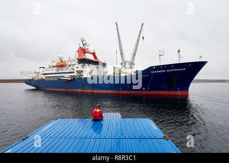 La France, les Terres Australes et Antarctiques Françaises (TAAF), îles Kerguelen, Port-aux-Français, à bord de la barge Aventure II, le seul bateau de l'île, qui transporte les marchandises lourdes (conteneur) entre le Marion Dufresne et l'embarcadère de Port-aux-Français. Un marin assis sur un conteneur lors de l'approche de la Marion Dufresne Banque D'Images