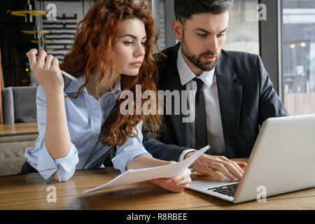 Businesspeople having business lunch au restaurant assis working on laptop holding documents Banque D'Images