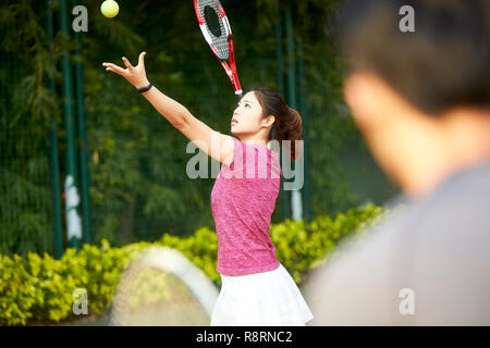 Jeune joueur de tennis asiatique de sexe féminin travaillant avec l'entraîneur sur le service Banque D'Images