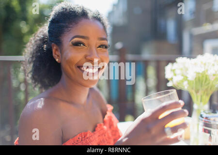 Portrait souriant et confiant woman drinking orange juice sur balcon ensoleillé Banque D'Images