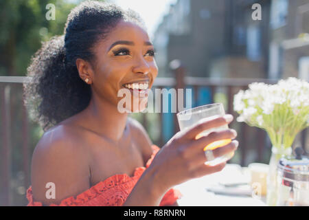 Happy young woman drinking orange juice sur balcon ensoleillé Banque D'Images