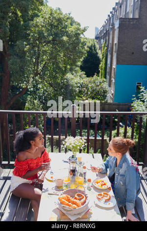 Les jeunes femmes friends enjoying brunch sur balcon ensoleillé appartement urbain Banque D'Images