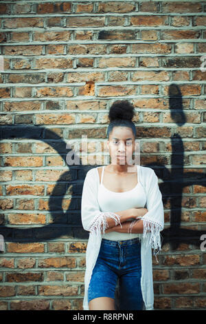 Portrait confiant, grave young woman leaning against brick wall Banque D'Images