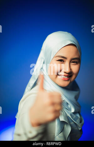 Portrait souriant, confiant jeune femme en soie bleu hijab gesturing thumbs-up Banque D'Images