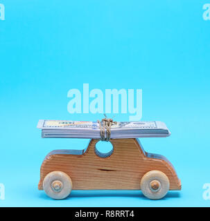 Petite voiture pour enfants en bois porte sur le sommet du toit d'une pile de billets en papier, un fond bleu Banque D'Images