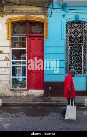 Homme cubain avec housse de transport à marcher le long des rues de La Havane à Cuba. La porte rouge correspond à la couleur de sa chemise. Banque D'Images