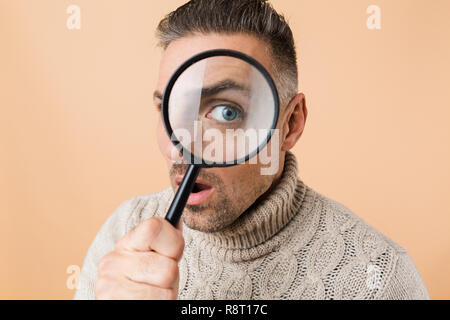 Close up of a choqué l'homme à travers une loupe isolated over beige background Banque D'Images