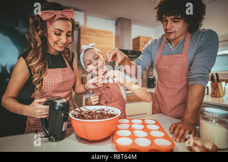 Heureux parents et leur fille sont en train de préparer des cookies ensemble dans la cuisine. Petite fille aide à ses parents avec le mélangeur. Banque D'Images