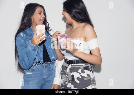 Laughing teenage Twin Sisters en utilisant des téléphones intelligents Banque D'Images