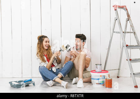 Photo de couple joyeux man and woman sitting on floor sur mur blanc près de l'échelle lorsque la rénovation de piscine Banque D'Images