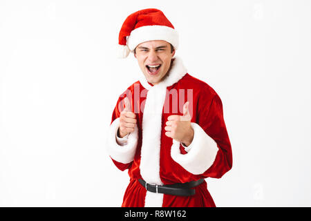 Portrait d'un homme 30s en costume de Père Noël et red hat laughing with Thumbs up isolé sur fond blanc en studio Banque D'Images