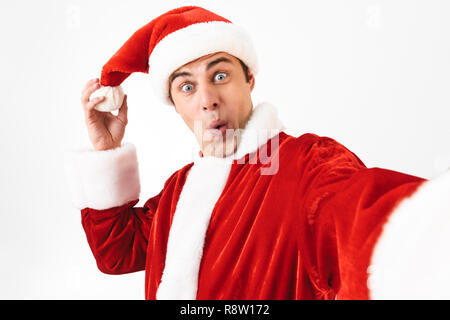 Portrait of cheerful man 30s en costume de Père Noël et red hat en riant tout en tenant plus isolés photo selfies fond blanc en studio Banque D'Images