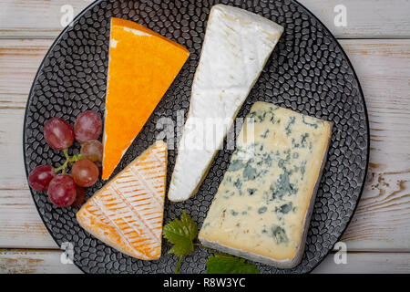 Plaque de dégustation avec quatre fromages, crème de brie France, marcaire, saint paulin et fromages d'auvergne bleu, servi avec des raisins mûrs close up Banque D'Images