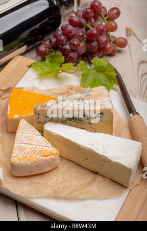 Plaque de dégustation avec quatre fromages, crème de brie France, marcaire, saint paulin et fromages d'auvergne bleu, servi avec des raisins mûrs close up Banque D'Images