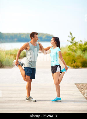 Smiling couple stretching jambes on beach Banque D'Images