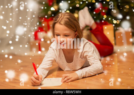 Smiling girl écrit la liste de souhaits de Noël à la maison Banque D'Images