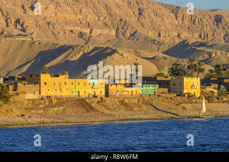 Vue d'un petit village typique au bord de bâtiments sur les rives du Nil, en Haute-Égypte, contre un arrière-plan de colline aride désert du Sahara Banque D'Images