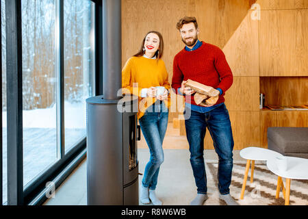 Portrait d'un jeune couple dans des pulls, debout près de la cheminée dans la maison moderne Banque D'Images
