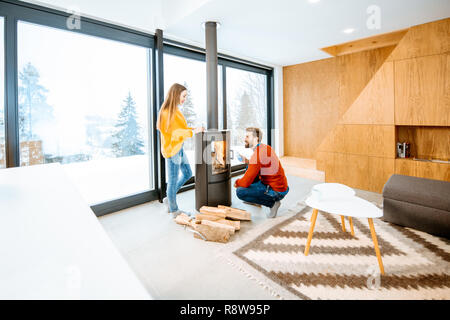 Jeune couple vêtus de chandails lumineux réchauffe près de la cheminée dans la maison moderne dans les montagnes pendant l'hiver Banque D'Images