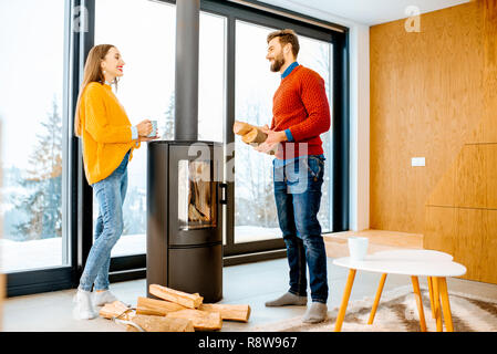 Jeune couple vêtus de chandails lumineux réchauffe près de la cheminée dans la maison moderne dans les montagnes pendant l'hiver Banque D'Images