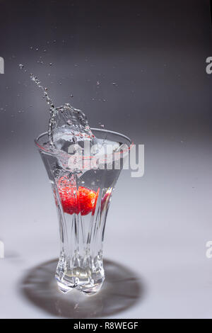 Un lumineux, fraise rouge tombe dans un vase de cristal rempli d'eau et crée un splash. Banque D'Images