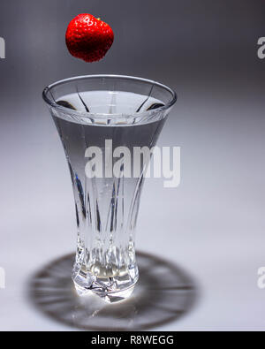 Un lumineux, fraise rouge tombe dans un vase de cristal rempli d'eau et crée un splash. Banque D'Images