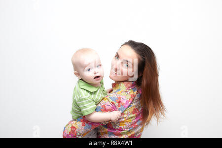 Jeune brunette maman, girl holding un petit bébé garçon dans ses bras qui s'ébattent. Ambiance familiale avec des sourires. famille heureuse sourit. Banque D'Images