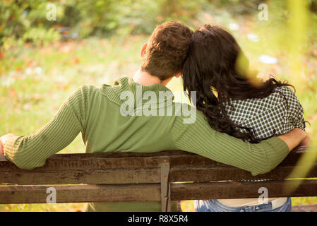 Photo d'un jeune couple, le dos tourné à la caméra, assis sur un banc, la tête penchée sur l'autre. Banque D'Images